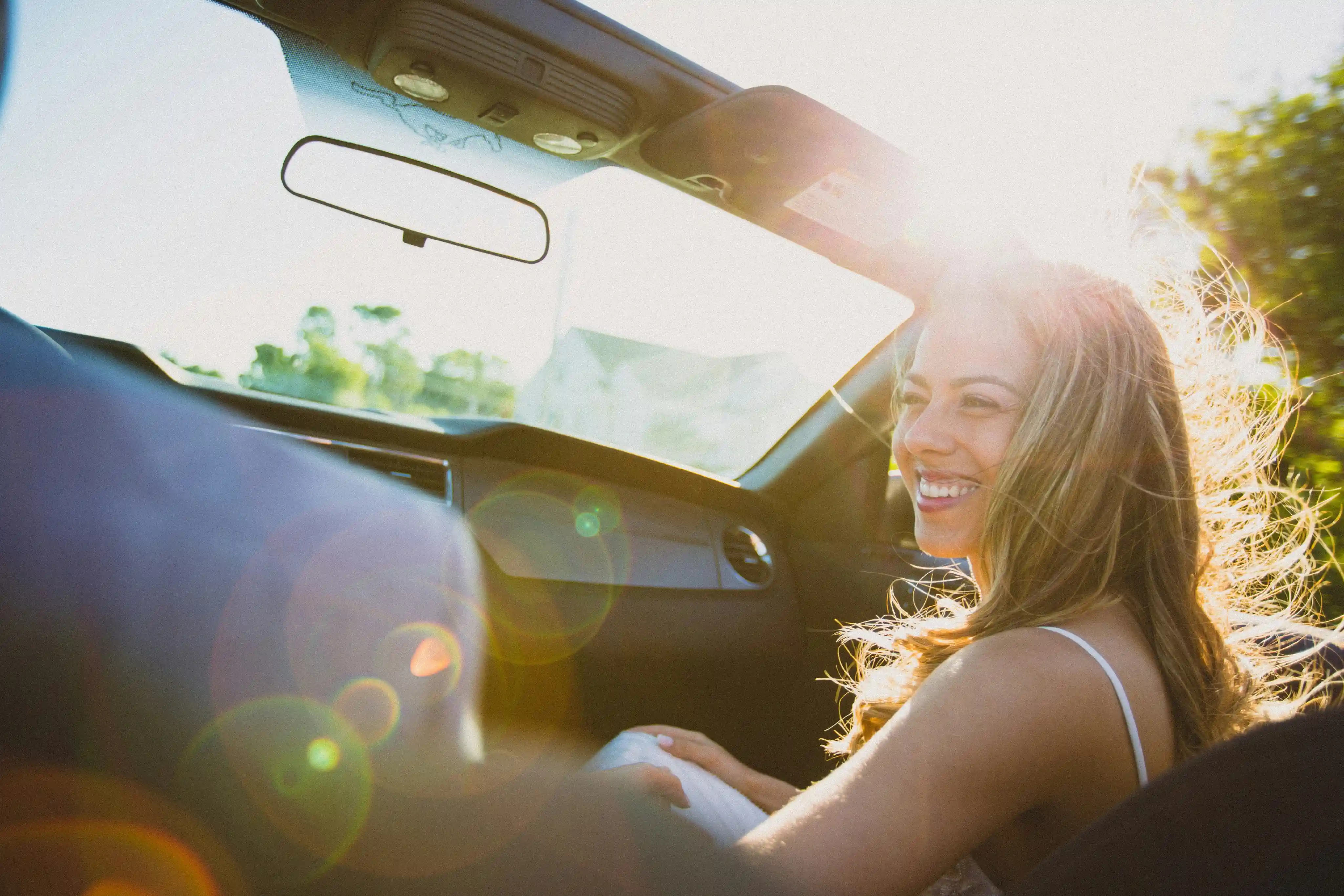 A smiling woman riding in the passenger seat of a convertible.